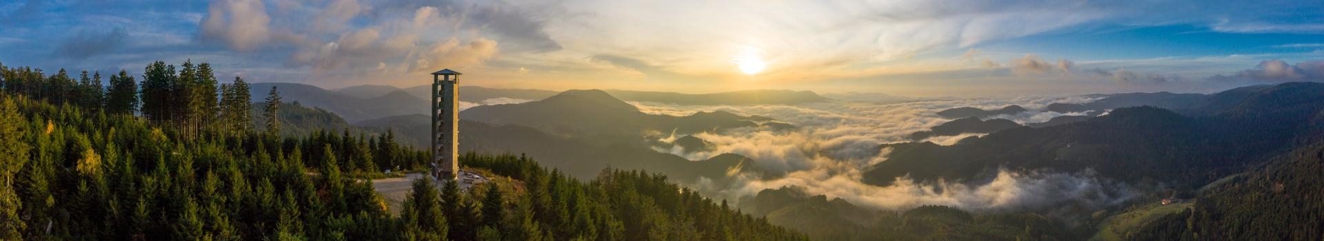 Blick über die Schwarzwaldberge mit dem Buchkopfturm auf der linken Seite. Im Hintergrund Sonnenschein und Nebelmeer